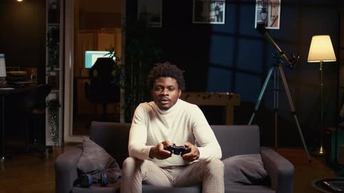 Young Adult Plays Video Games at Home on Couch