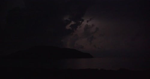 Summer thunderstorm in night dark sky with clouds over an island.