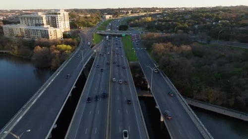 Aerial view following cars and traffic as they commute and cross highway bridge over a river. Drone