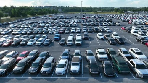 Aerial truck shot of vehicles parked in Manheim Auto Auction parking lot. Sun reflects off of shiny