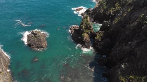 Aerial drone flying over big sharp rocks near a paradise coast. Waves crashing, blue water.