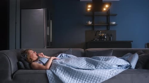 Une femme malade de la grippe tousse et se mouche sous une couverture sur un canapé à la maison, jeune caucasienne
