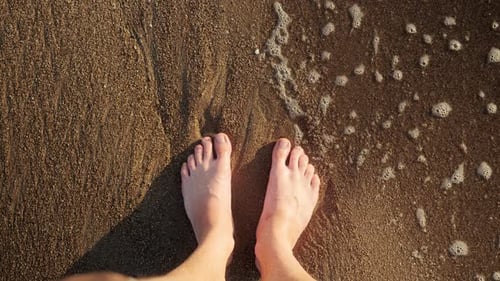 Waves Wash Men's Feet on a Sandy Beach