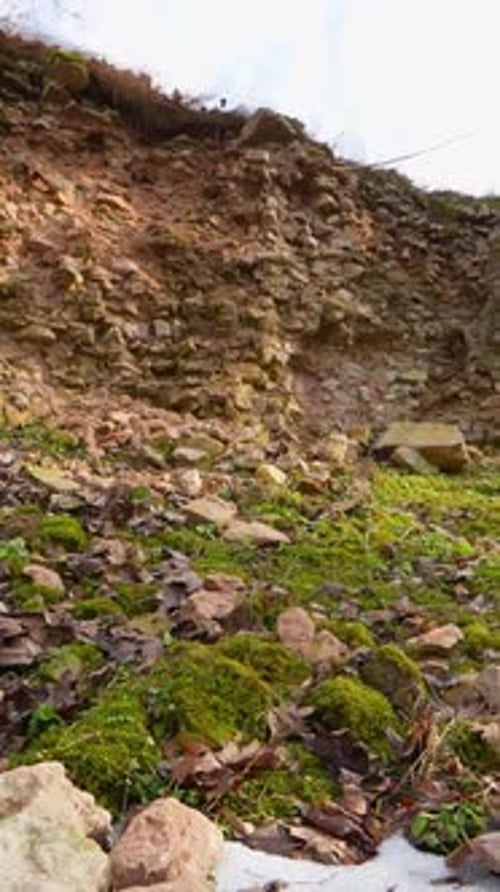 Vertical view of a crumbling historic stone wall with fallen masonry, moss, and exposed earth,