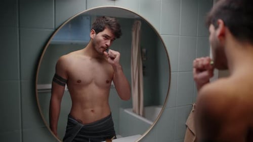 Man Brushing His Teeth In Front Of The Bathroom Mirror