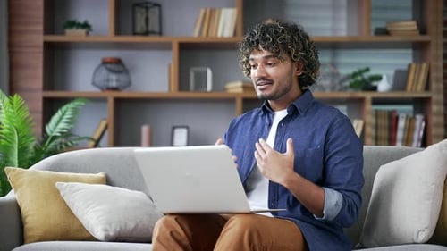 Webcam view. Young man talking on a video call looking at camera sitting on sofa in living room