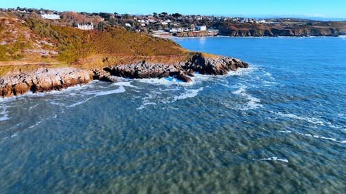A rocky coastline extends into the blue ocean with waves crashing against the shore.