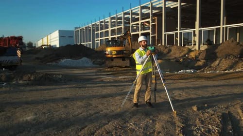 A Construction Worker is Carefully Surveying the Site with Leveling Tools for Accurate Planning