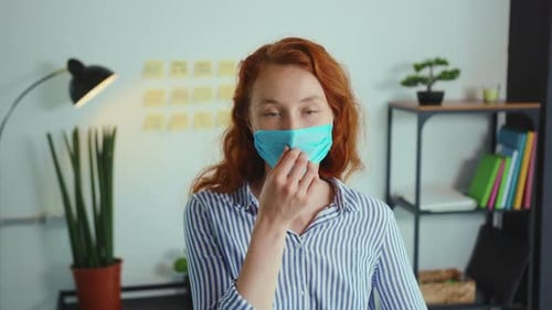 Smiling Woman Employee in a Medical Facial Mask Works in the Office Look at Camera Coronavirus