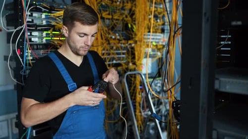 Junger Mann in Uniform testet Internetausrüstung mit einem speziellen Gerät im Serverraum