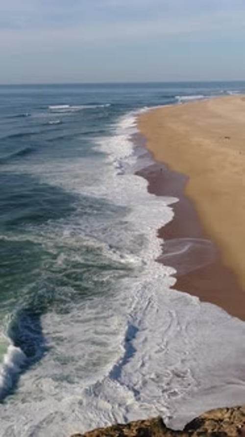 Waves of the Atlantic Ocean on Nazare Beach with a rocky cliff in the background in Nazare, Portugal