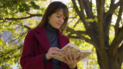 An Attractive Middleaged Caucasian Woman Reads a Book with a Smile in a Park Closeup From Below