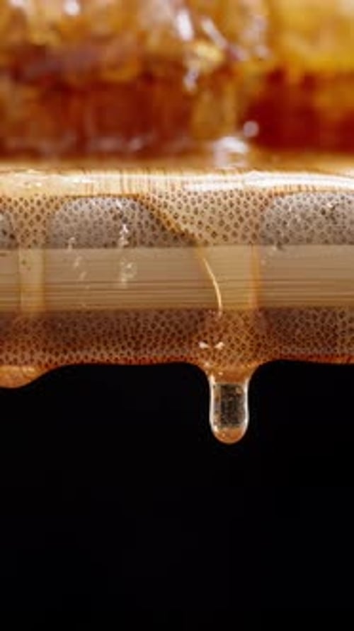 Vertical video. Natural honey in honeycomb on a wooden board from which its drops are falling down.