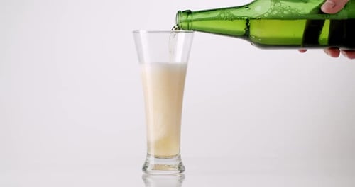 Hand Pouring Cold Fresh Beer Into a Glass From a Green Bottle