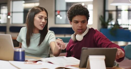 Étudiants afro-américains au bureau, femme penchée, pointant du doigt la tablette, homme ajustant et étudiant un livre