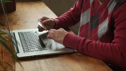 Man uses laptop with credit card indoors
