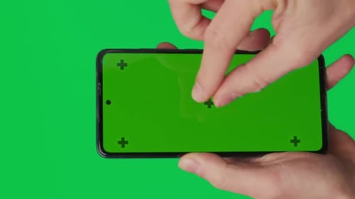 Male Hand Holding a Smartphone with Vertical Green Chroma Key Screen Isolated on Green Background