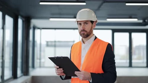 Professional Engineer in Safety Vest and Helmet Inspects Construction Site with Clipboard and Smiles