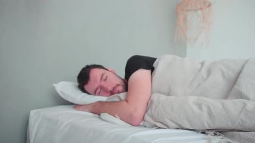 Homme endormi, blanc de race blanche avec barbe, jeune homme couché dans son lit en train de rêver, pi mal à l'aise