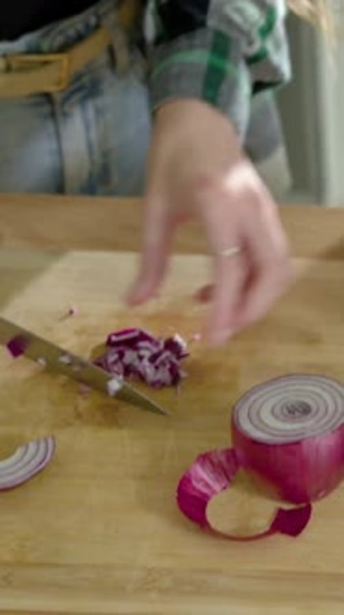Vertical video: Dicing halved red onion, plaid cook preparing meal on board with knife in kitchen