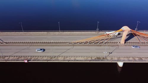 Drohnenaufnahme einer kleinen Hängebrücke über einen Fluss mit vorbeifahrenden Autos von oben nach unten. Städtische Informationen