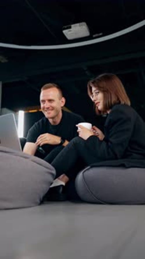 Young male and female co-workers sit in bean bag chairs communicating cheerfully.