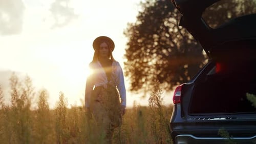 At Sunlight Young Woman with Hat Walking Near Her Car Enjoying Sunset View in Field Expression