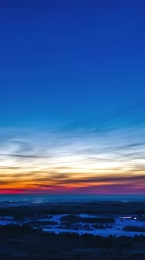 Ciel crépusculaire coloré au-dessus de la campagne enneigée avec des lumières lointaines