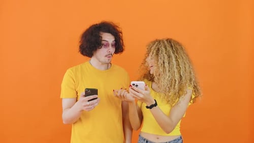 Young Couple Laughing at Smart Phone on Orange