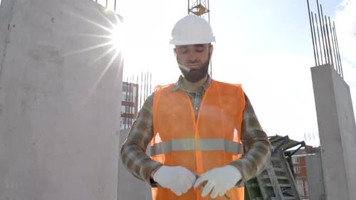 Builder repairman in protective helmet and vest stands at workplace in building and holds ruler