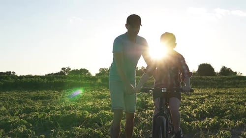 A Happy Family Father Teaches His Son to Ride a Bike in the Park