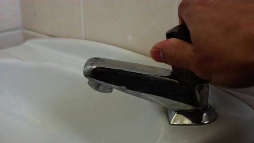 footage of hand twisting the faucets to run the water on a dirty sink.