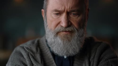 Contemplative man with gray beard looking down, close-up