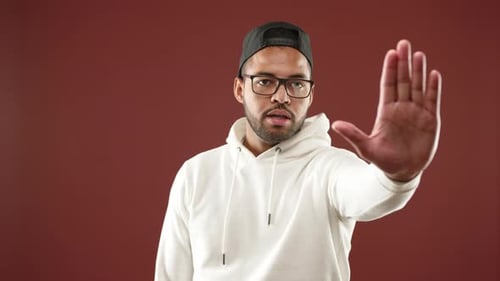 Man Assertively Gesturing Stop with Hand in a White Hoodie and Cap