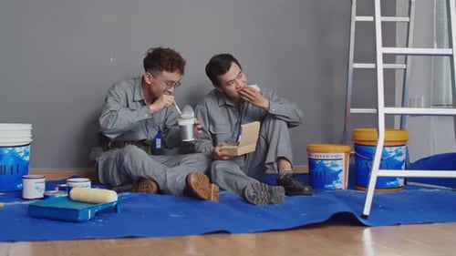 Builders Sitting on Floor and Eating Lunch at Construction Site