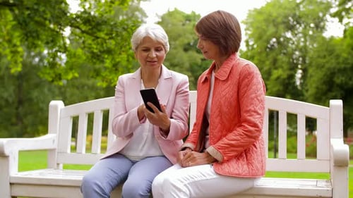 Two women sitting on a bench using smartphone