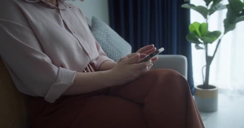 A Woman is Typing on a Mobile Phone Screen and Chatting While Sitting on the Sofa The Girl Uses the