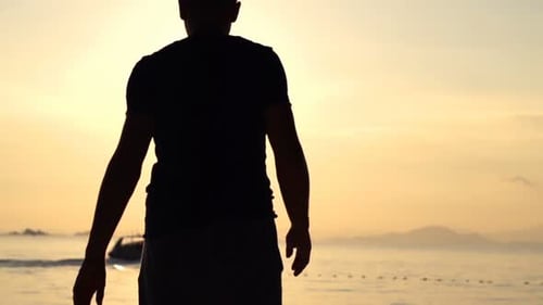 Silhouette of man walking on beautiful beach at sunset enjoying summer vacation