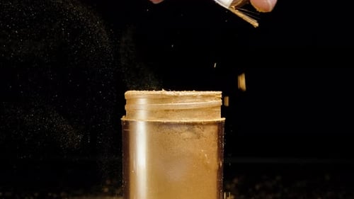 Using a brush, I disperse golden dust into the air, in slow motion against a black background.
