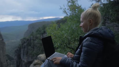 Female Freelance Sits on the Edge of a Cliff or Canyon with a Laptop and Works