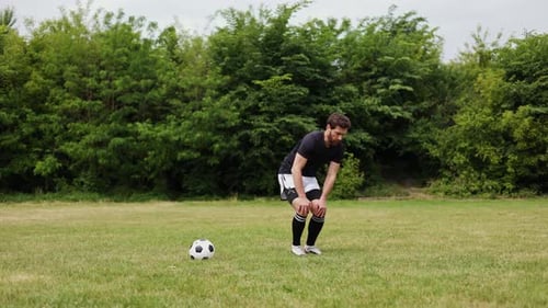 Young Man Stretching on Grassy Field with Soccer Ball Positioned Nearby