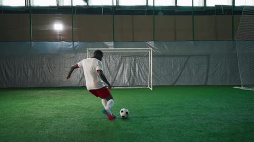 Jugador de fútbol negro ejerciendo penalti en la sala de entrenamiento marcando un gol: Vista posterior