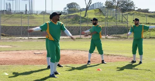 Training cone initiating diverse baseball players rotating arms forward and back warming on infield