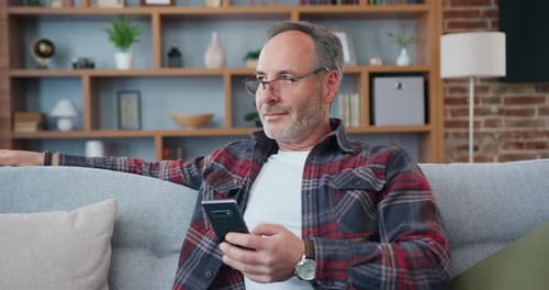 Man Relaxing on Couch Using Smartphone at Home