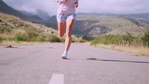 Young Woman Runs a Mountain Road Swiftly Covering Distance with Mountains Ahead
