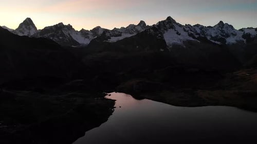 Aerial flyover over an alpine lake after an autumnn sunset with a colorful glow behind the dark Alps