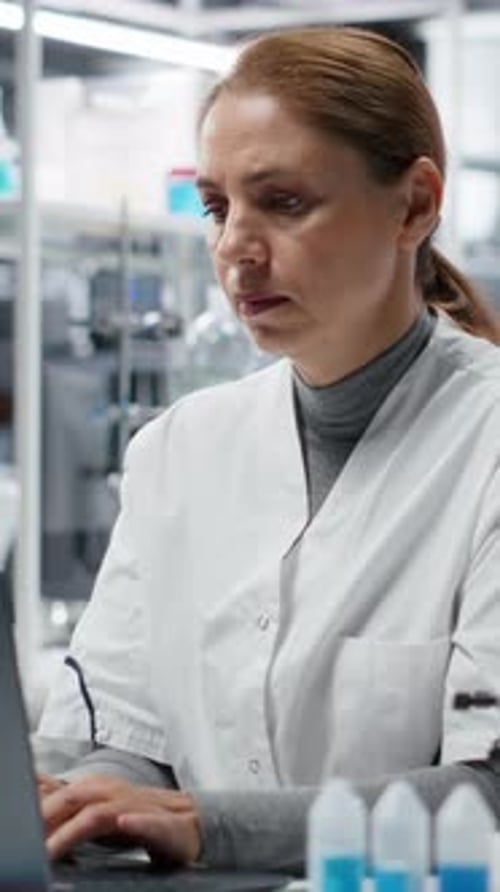 Woman Lab Worker Typing On Laptop Then Rubs Temples