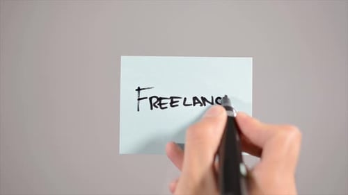Hand Writes Freelancer on Blue Sticky Note