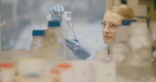Woman in Lab Coat Pouring Liquid in Beaker