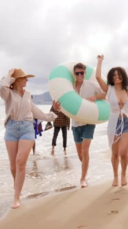 Cheerful friends running together on the beach during summer vacation